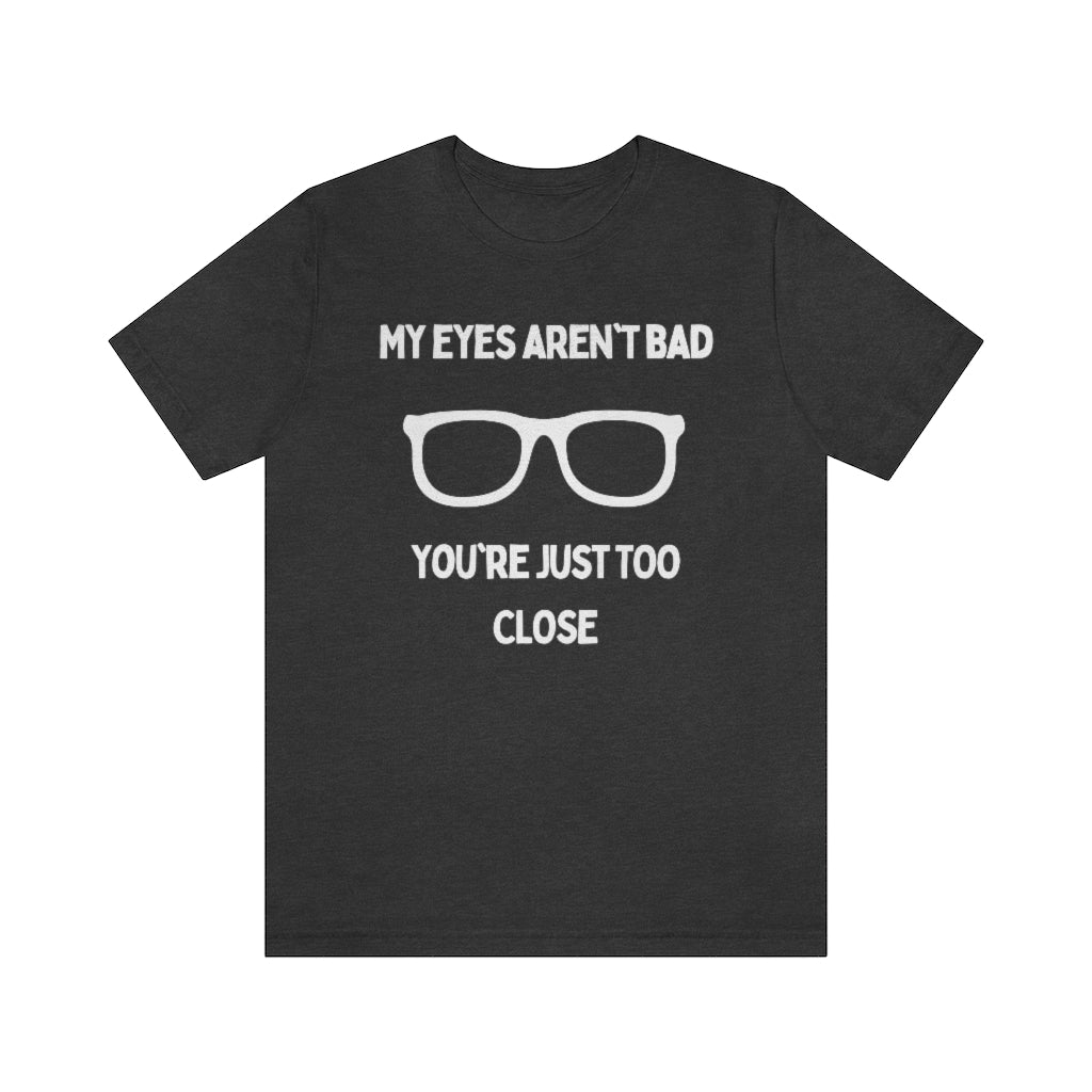 A dark grey heather t-shirt with white text reading "My eyes aren't bad, you're just too close" with a pair of glasses in the middle.