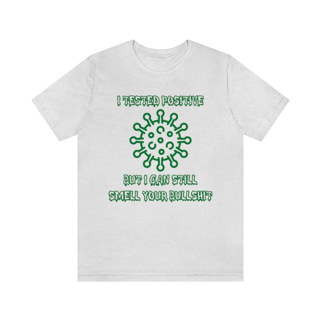 An ash-colored t-shirt with green, sickness-dripping text and a corona virus image saying "I tested positive, but I can still smell your bullshit"