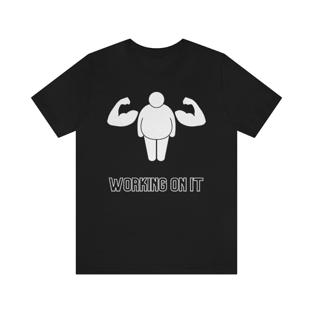 A black t-shirt showing a fat stickfigure with an extra set of muscular arms. Under it reads: "Working on it".