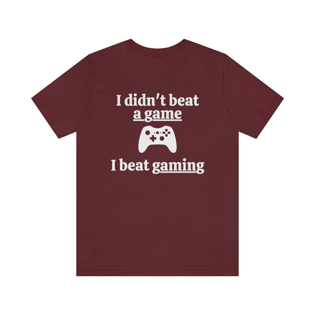Maroon t-shirt with white text saying "I didn't beat a game, I beat gaming". With an iamge of an xbox controller in the middle.