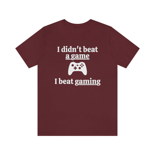 Maroon t-shirt with white text saying "I didn't beat a game, I beat gaming". With an iamge of an xbox controller in the middle.