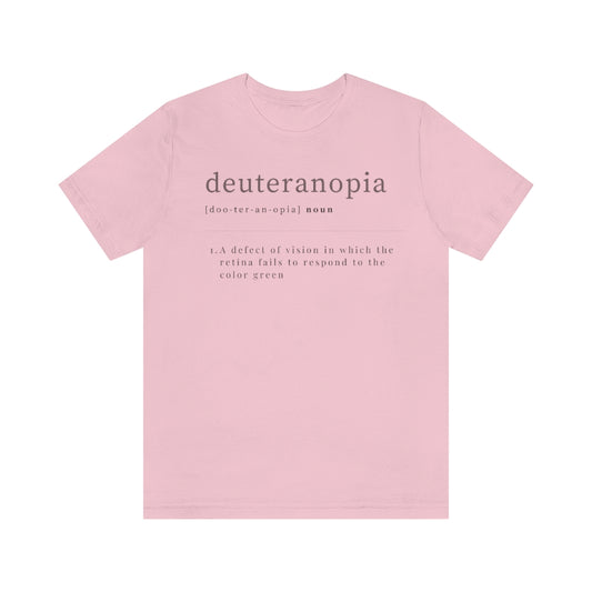 A pink t-shirt with text laid out like a dictionary. It reads in black letters: "Deuteranopia, noun. A defect of vision in which the retina fails to respond to the color green."