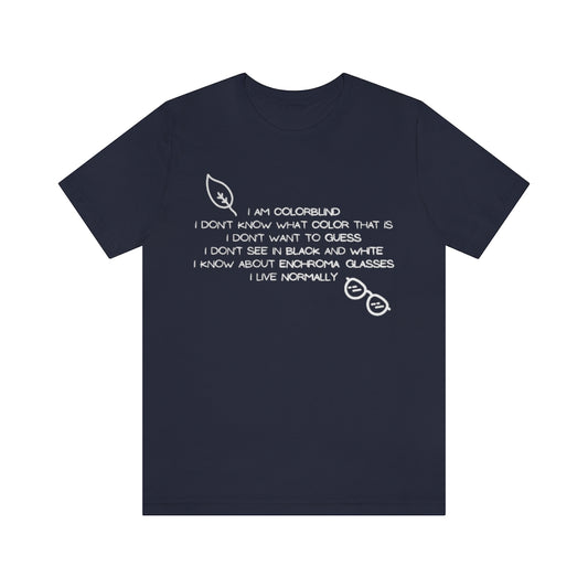 A navy colored t-shirt with white text reading: I am colorblind. I don't know what color that is. I don't want to guess. I don't see in black and white. I know about enchrroma glasses. I live normally. The top left has a drawing of a leaf, the bottomright a pair of sunglasses, both in white.