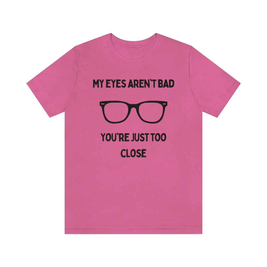 A charity pink t-shirt with black text reading "My eyes aren't bad, you're just too close" with a pair of glasses in the middle.