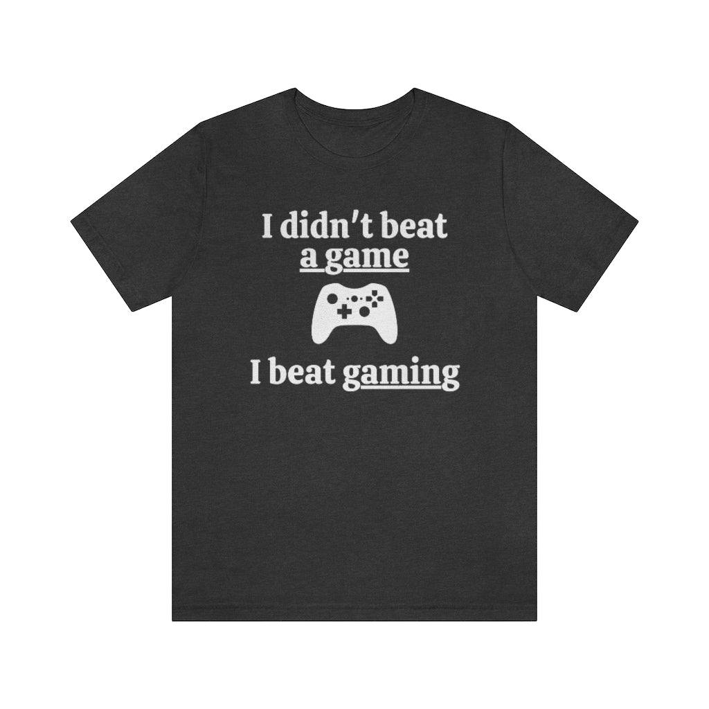 A dark grey heather t-shirt with white text saying "I didn't beat a game, I beat gaming". With an iamge of an xbox controller in the middle.