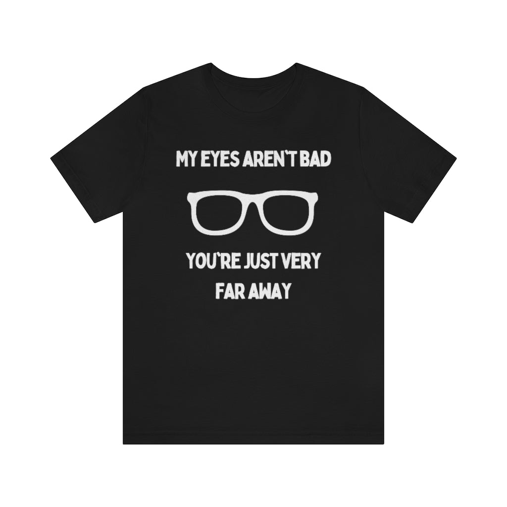 A black t-shirt with white text reading "My eyes aren't bad, you're just very far away" with a pair of glasses in the middle.
