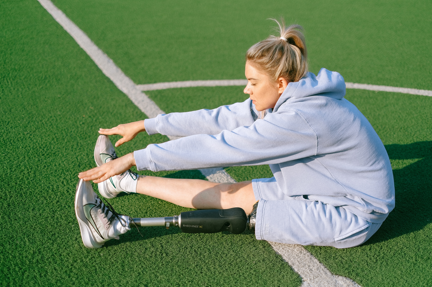 A young woman with a prosthetic right leg stretching on a sports field