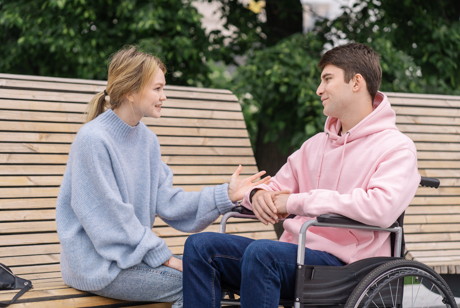 A girl sitting on a bench talking to a guy sitting in a wheelchair