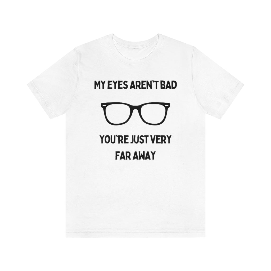 A white t-shirt with black text reading "My eyes aren't bad, you're just very far away" with a pair of glasses in the middle.
