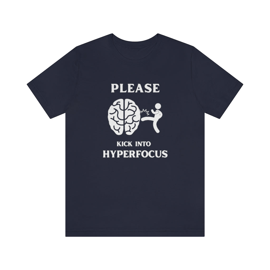 A navy t-shirt with white text saying "Please kick into hyperfocus". The world 'Please" at the top and inbetween the text is a stickfigure kicking a brain.