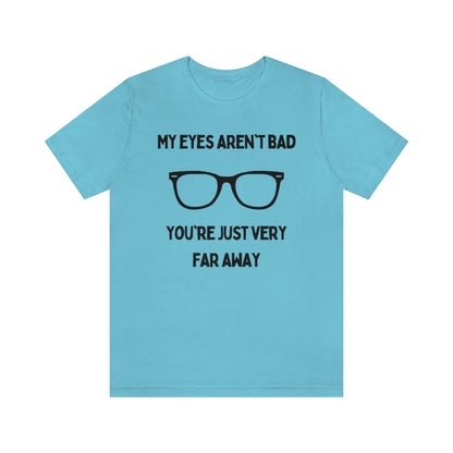 A turquoise t-shirt with black text reading "My eyes aren't bad, you're just very far away" with a pair of glasses in the middle.