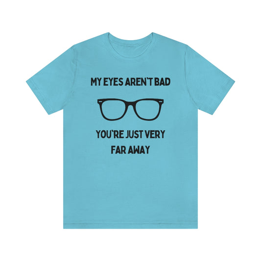 A turquoise t-shirt with black text reading "My eyes aren't bad, you're just very far away" with a pair of glasses in the middle.