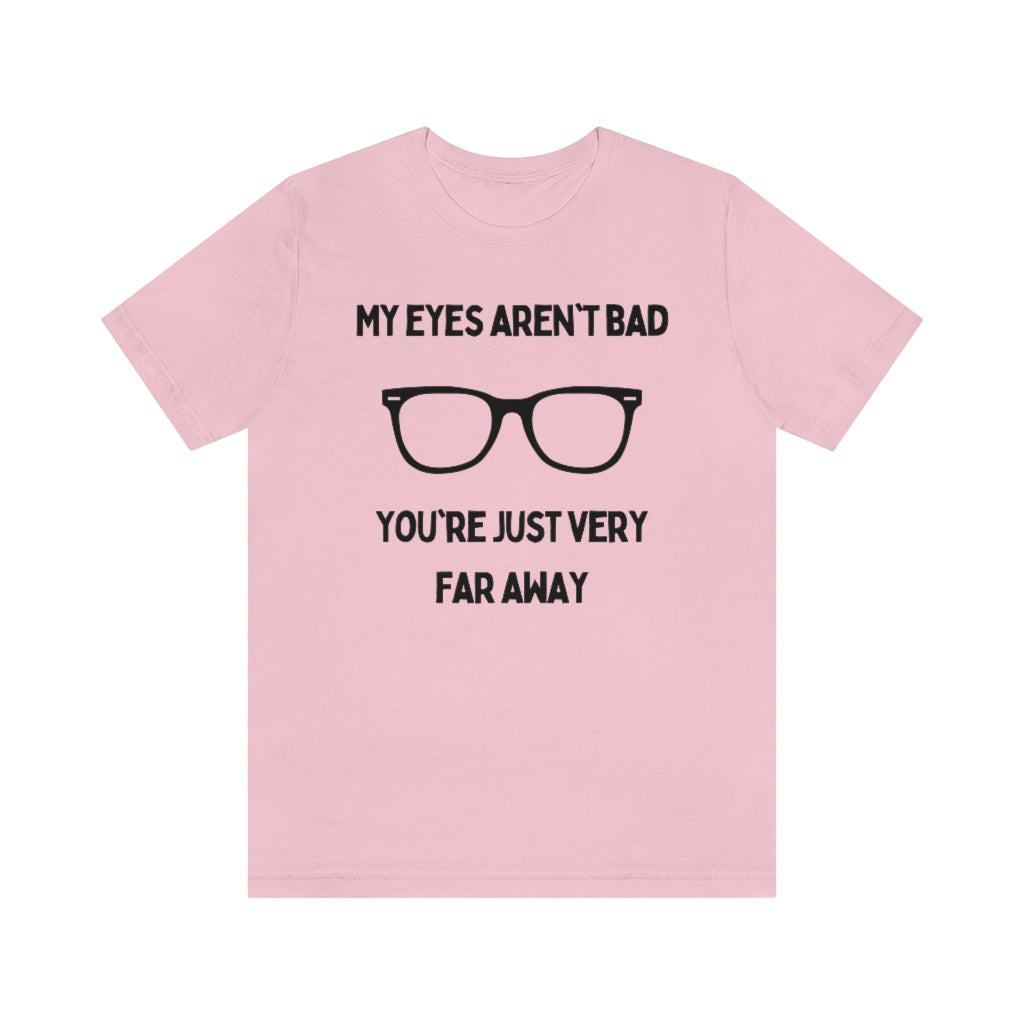 A pink t-shirt with black text reading "My eyes aren't bad, you're just very far away" with a pair of glasses in the middle.