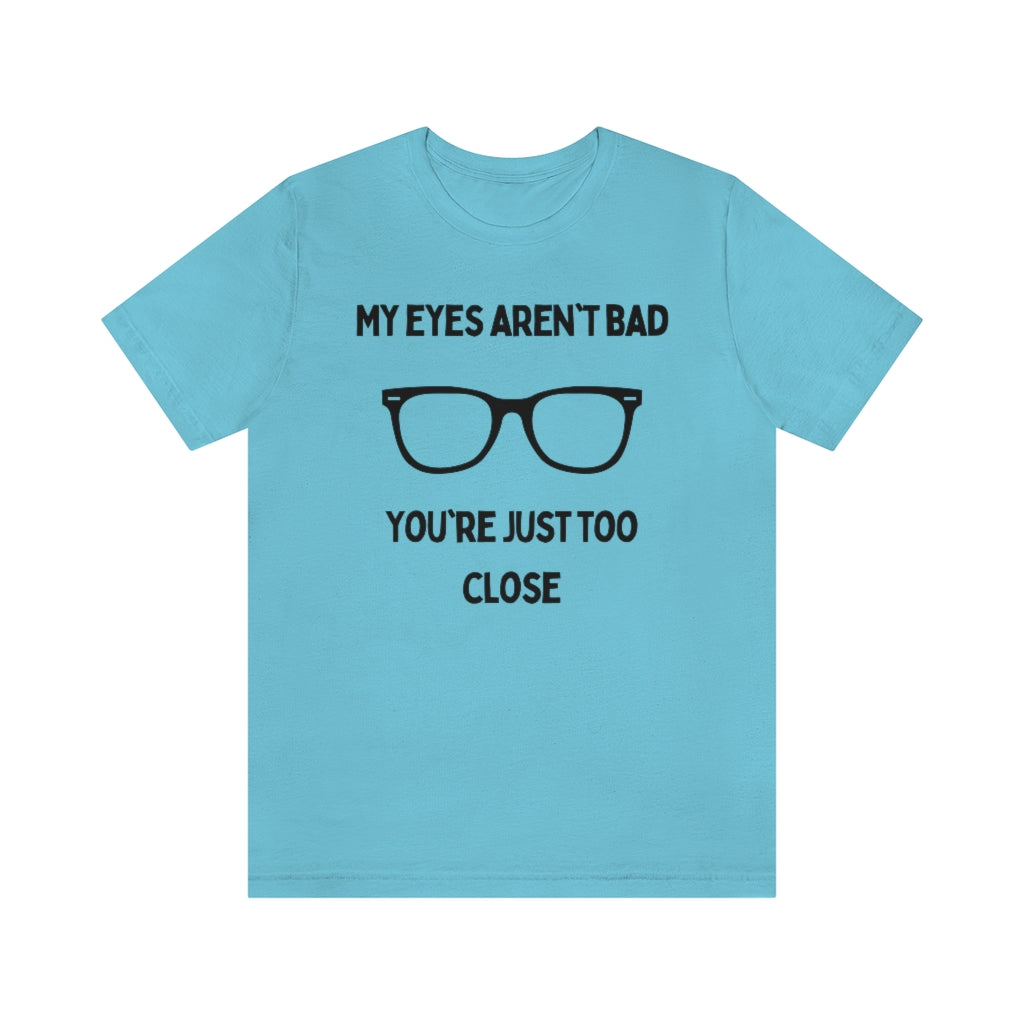 A turquoise t-shirt with black text reading "My eyes aren't bad, you're just too close" with a pair of glasses in the middle.