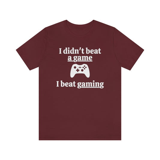 Maroon t-shirt with white text saying "I didn't beat a game, I beat gaming". With an iamge of an xbox controller in the middle. 