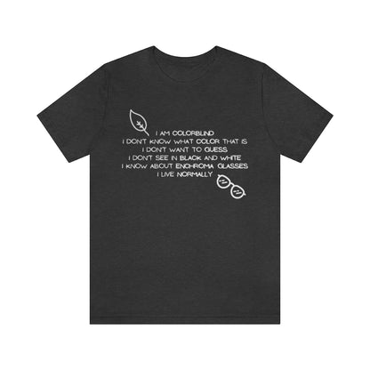 A dark gray heather colored t-shirt with white text reading: I am colorblind. I don't know what color that is. I don't want to guess. I don't see in black and white. I know about enchrroma glasses. I live normally. The top left has a drawing of a leaf, the bottomright a pair of sunglasses, both in white.