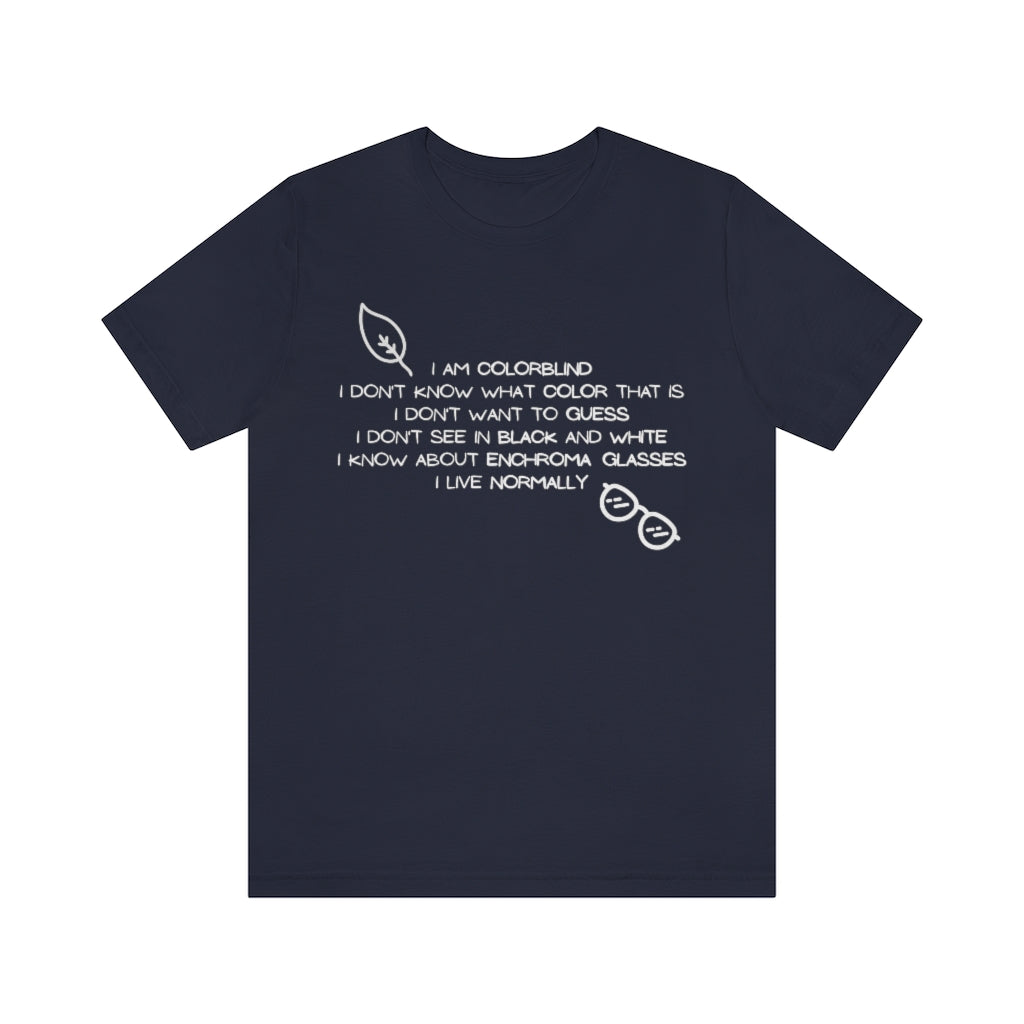 A navy colored t-shirt with white text reading: I am colorblind. I don't know what color that is. I don't want to guess. I don't see in black and white. I know about enchrroma glasses. I live normally. The top left has a drawing of a leaf, the bottomright a pair of sunglasses, both in white.
