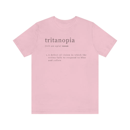 A pink t-shirt with text laid out like a dictionary. It reads in black letters: "Tritanopia, noun. A defect of vision in which the retina fails to respond to blue and yellow.