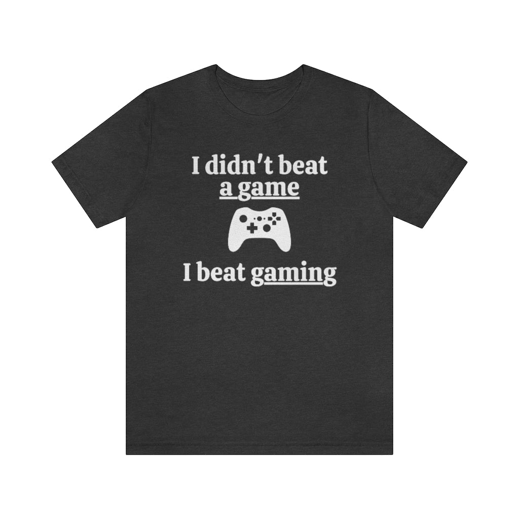 A dark grey heather t-shirt with white text saying "I didn't beat a game, I beat gaming". With an iamge of an xbox controller in the middle. 