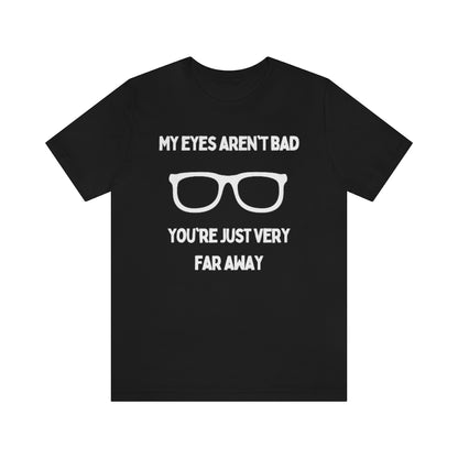 A black t-shirt with white text reading "My eyes aren't bad, you're just very far away" with a pair of glasses in the middle.